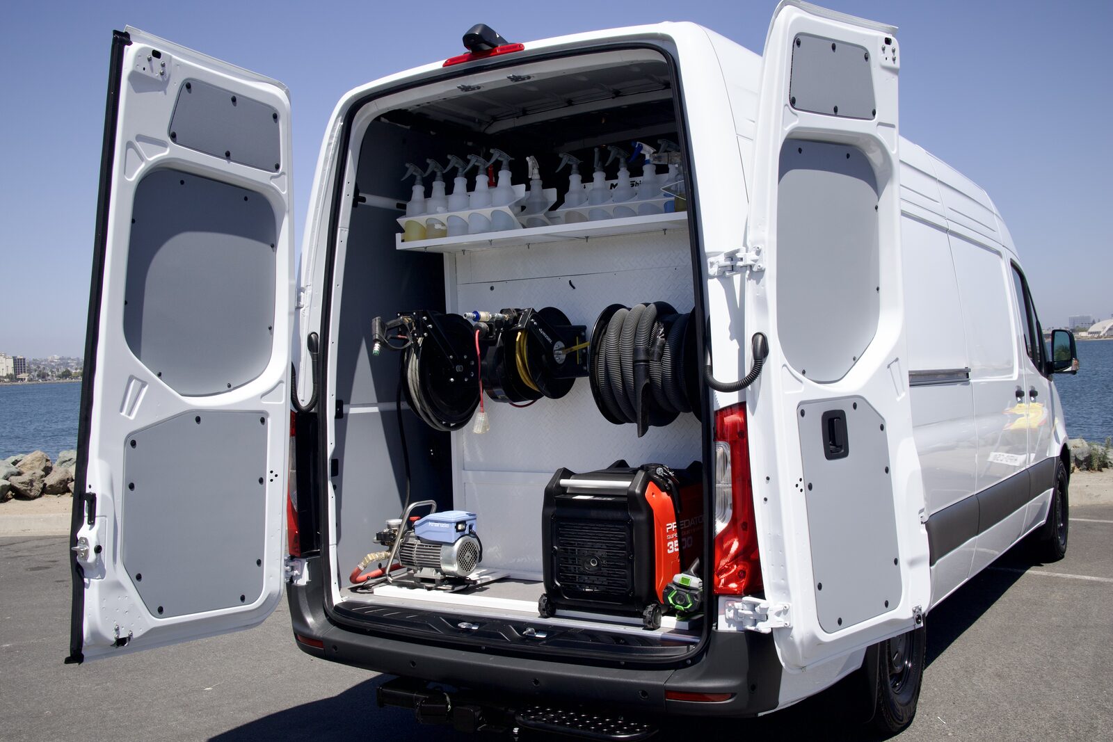 Rear of the DETL Sprinter van open, showing the organized detailing setup — professional products, hose reels, pressure washer and power station